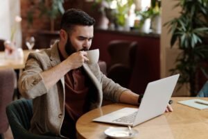 man drinking coffee while looking at his laptop